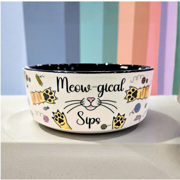 Ceramic pet bowl with cat-themed design and 'Meow-gical Sips' text on it.