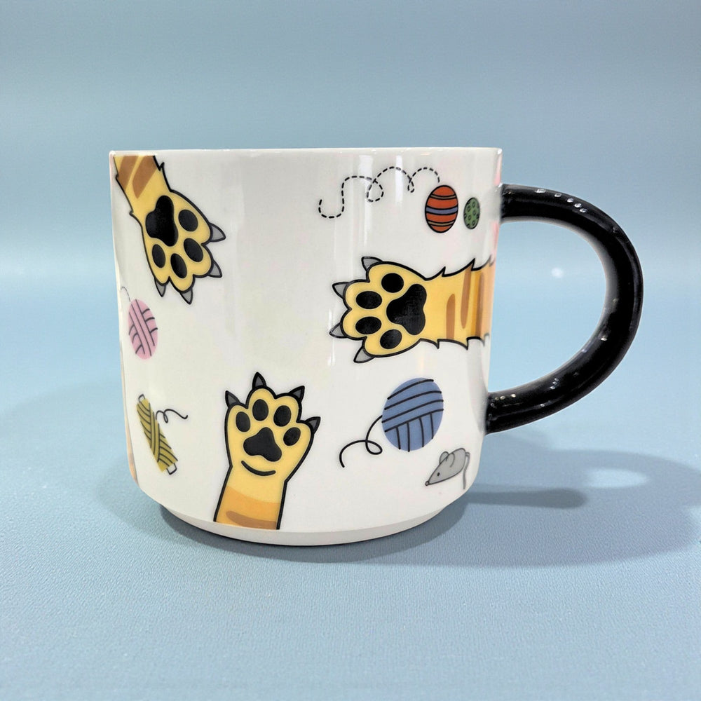 White ceramic mug with black handle featuring cartoon cat paw prints and other cat themes