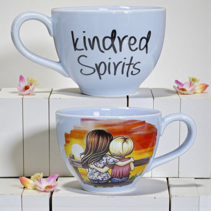 Front and back of one mug with front text reading'kindred Spirits' and the back with an illustration of two children hugging and watching a sunset.