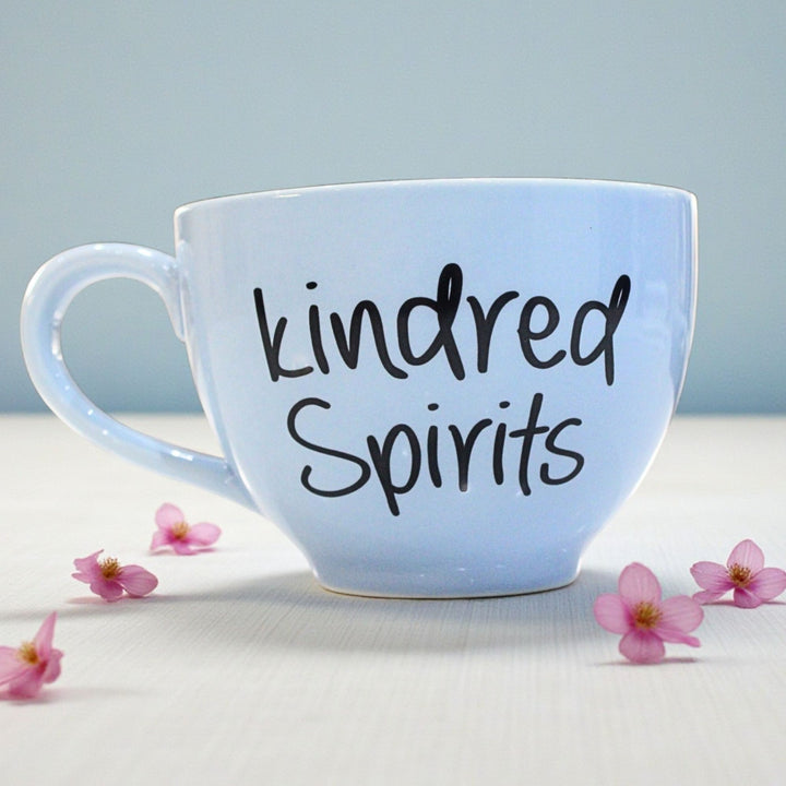 Light blue mug with 'kindred Spirits' text on a light surface with pink flowers.