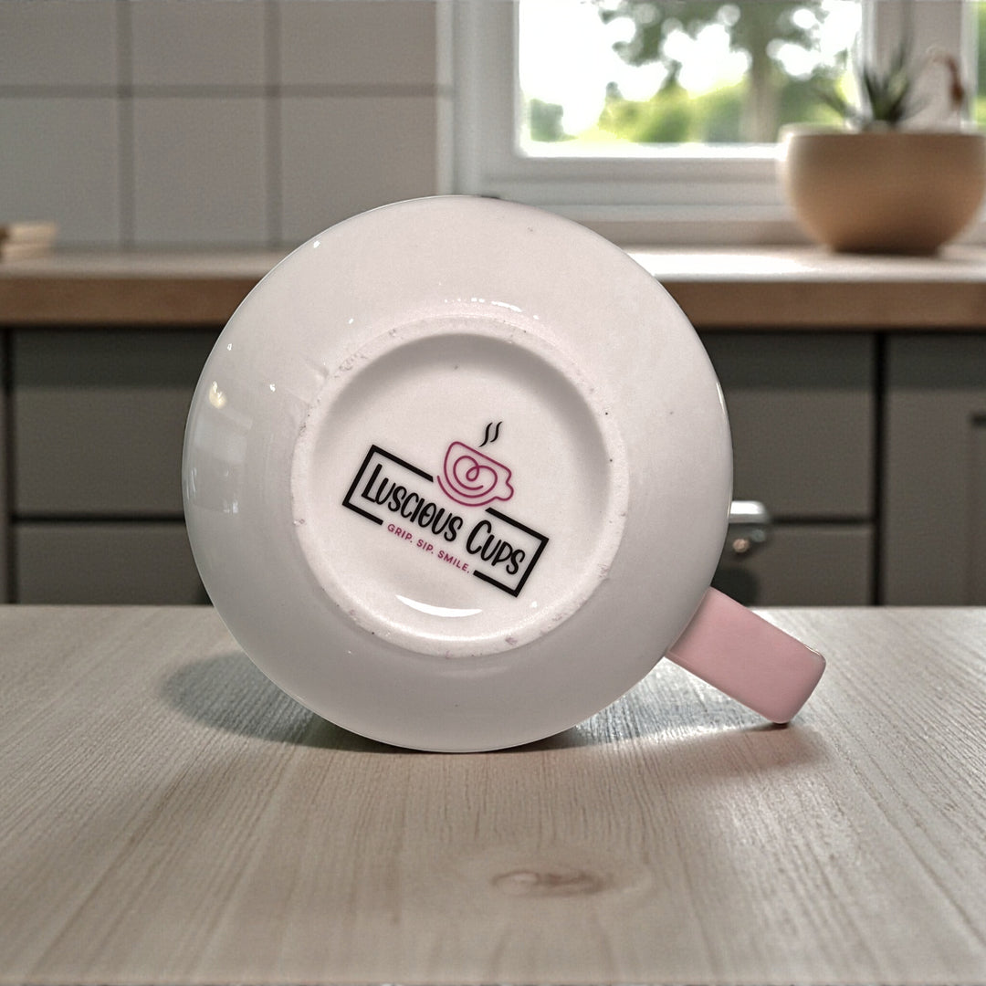 White mug with pink handle on a wooden surface, featuring 'Luscious Cups' logo.