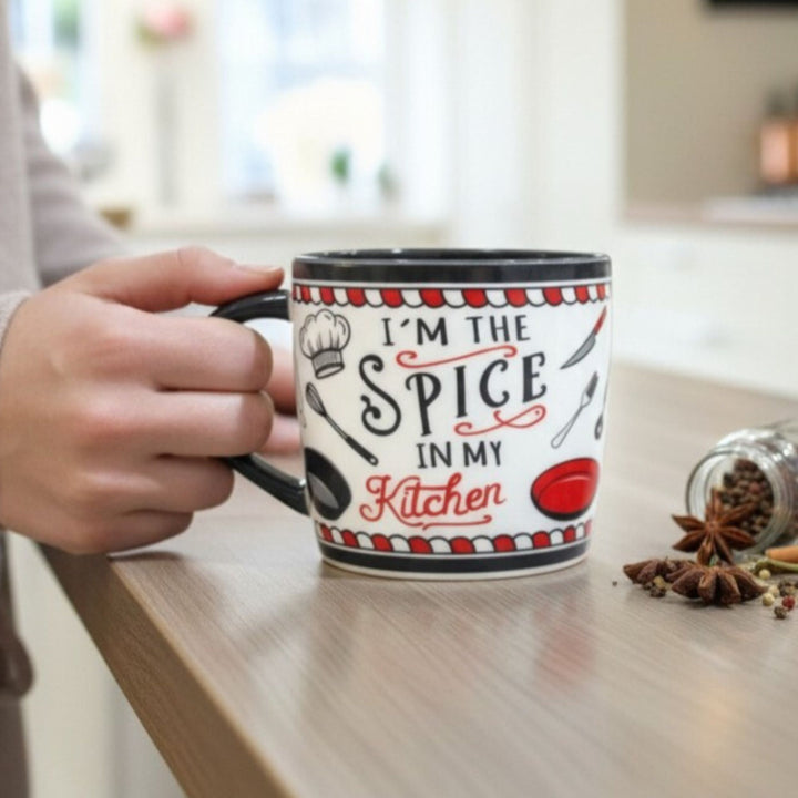 Person holding a mug with 'I'm the Spice in my Kitchen' text in a kitchen setting