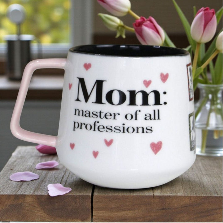 White mug with pink handle and heart designs, featuring text 'Mom: master of all professions'.